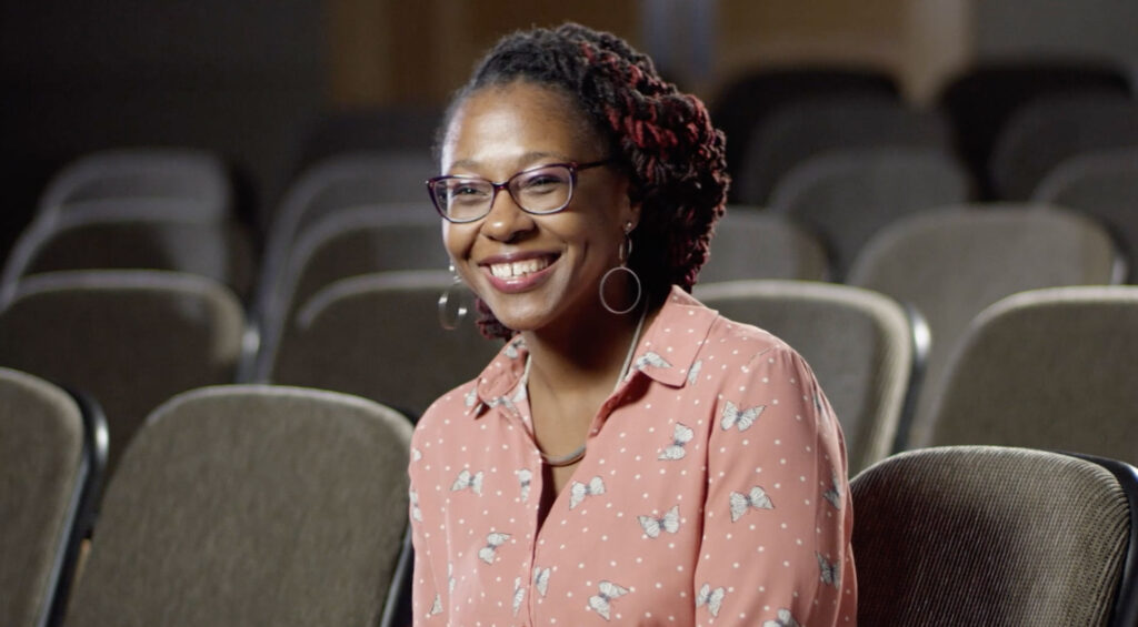 A smiling woman sits in an auditorium